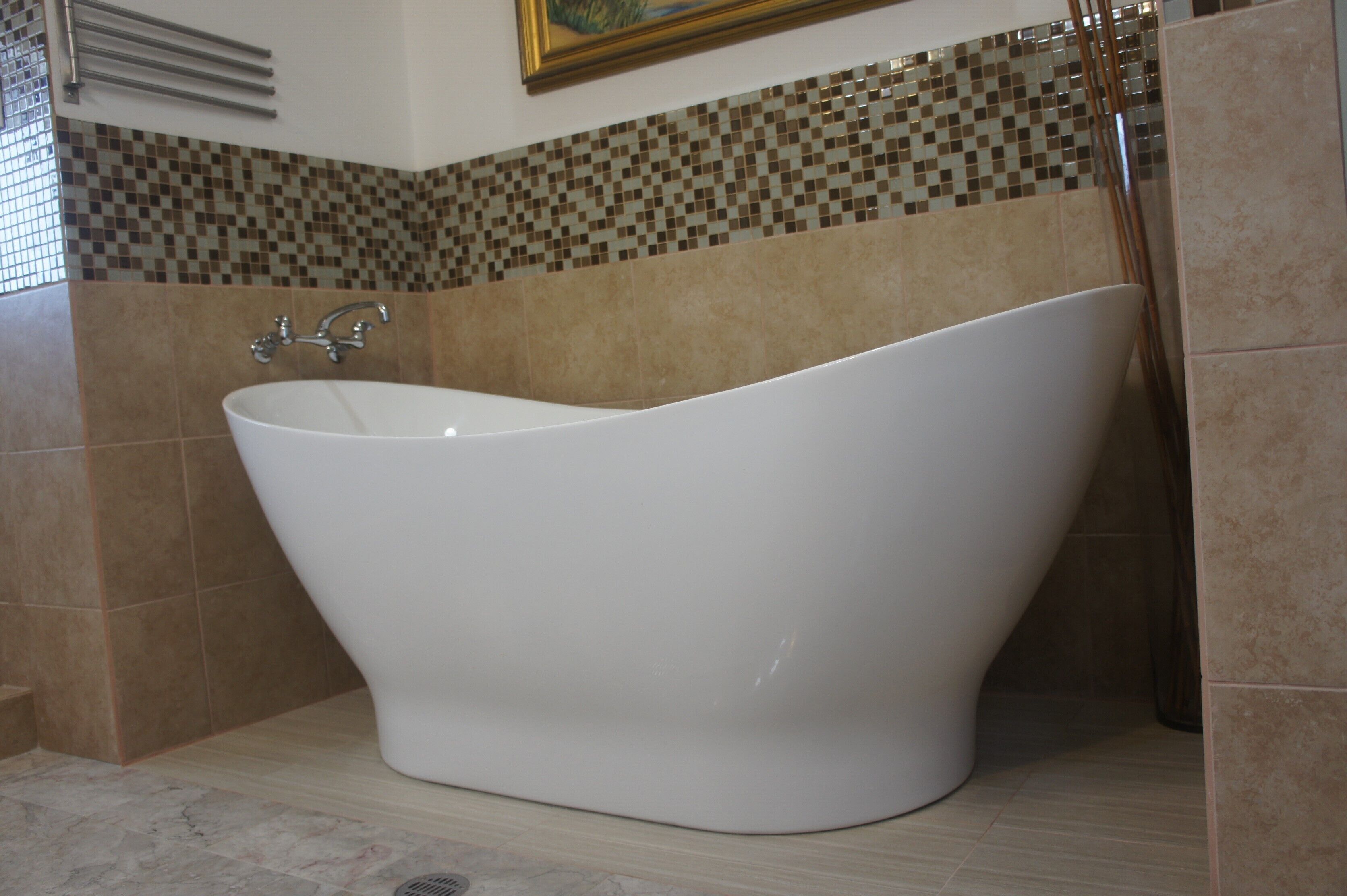 A freestanding bathtub in a bathroom with mosaic tile walls and a tiled floor.