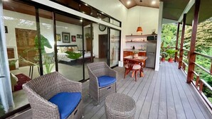 Um espaço de estar moderno com varanda, móveis de vime, cozinha e vista para o verde.