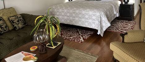Un dormitorio bien amoblado con una cama grande, dos mesitas de noche con lámparas, un sofá y una mesa de centro con una planta y controles remotos.