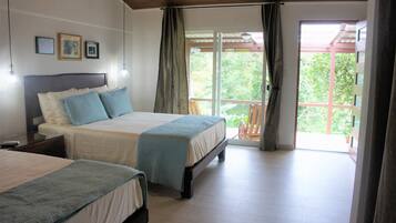 A bedroom with two beds, a balcony, and a view of greenery.