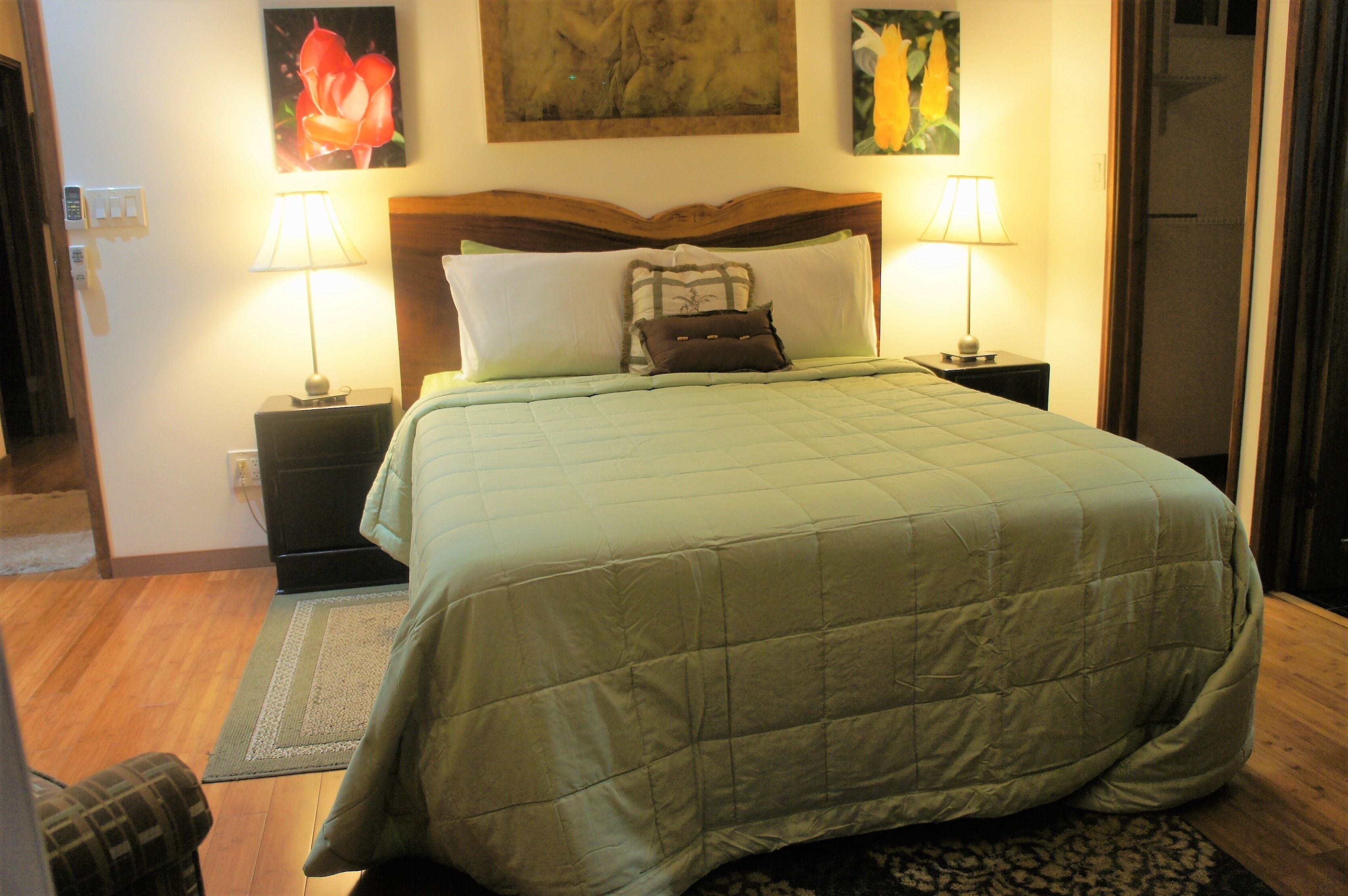 A neatly made bed with a green quilt, two bedside lamps, and a wooden headboard.