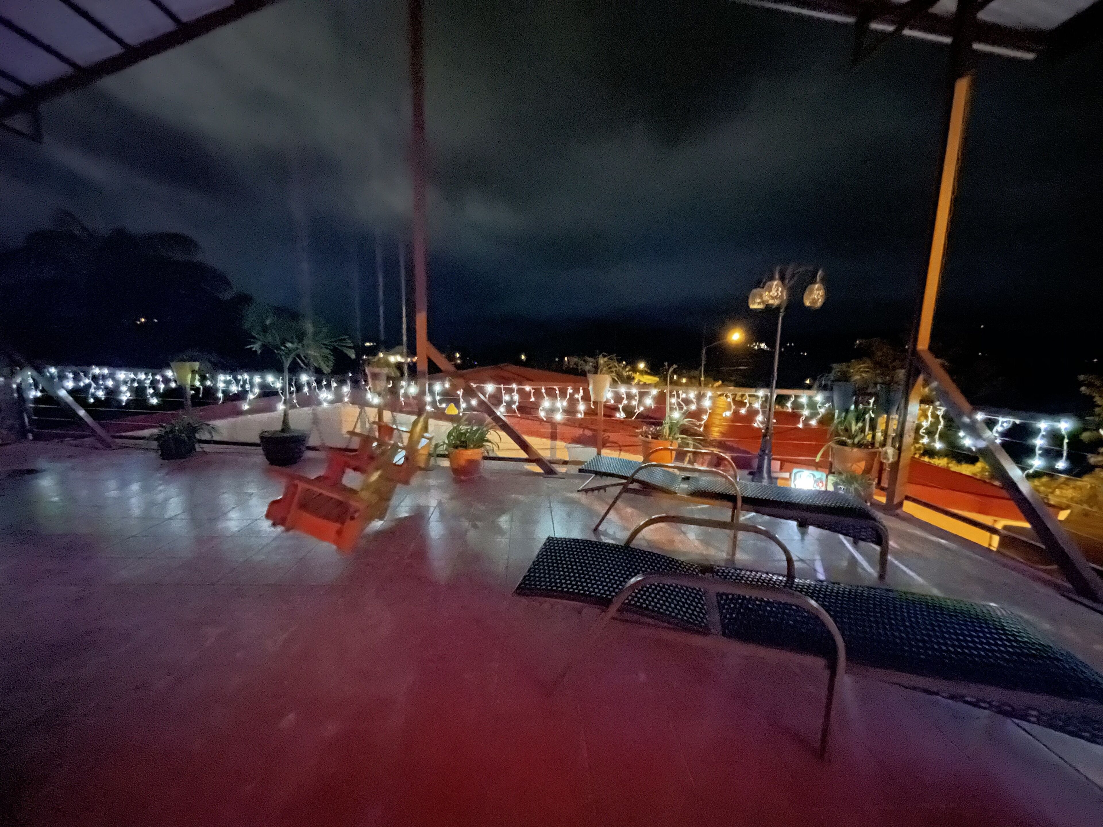 A covered outdoor seating area with chairs and tables, potted plants, and string lights.