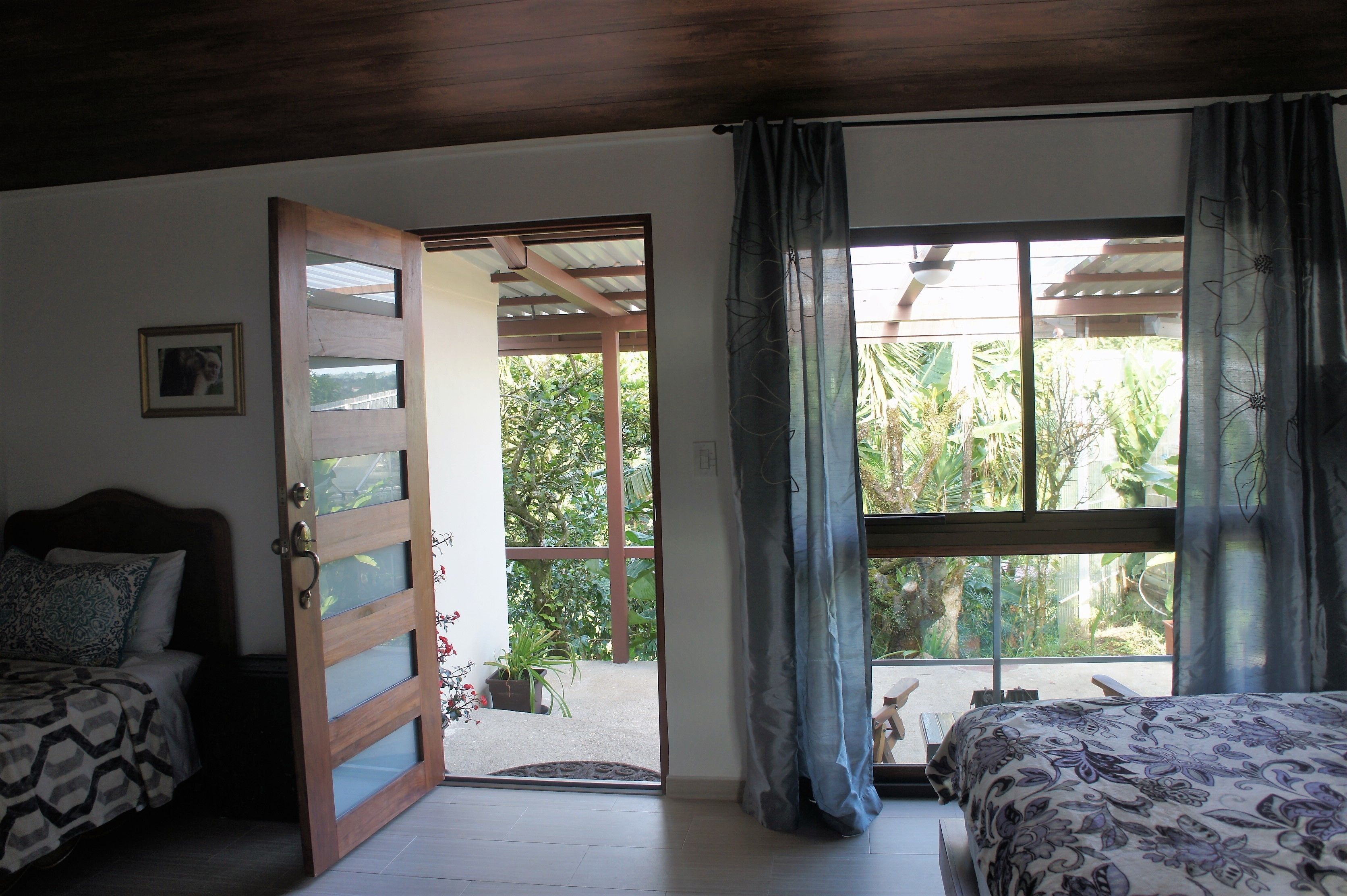 Una habitación con una cama, una puerta de madera y un ventanal con cortinas.