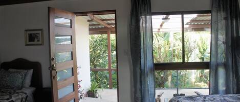 Una habitación con una cama, una puerta de madera y un ventanal con cortinas.