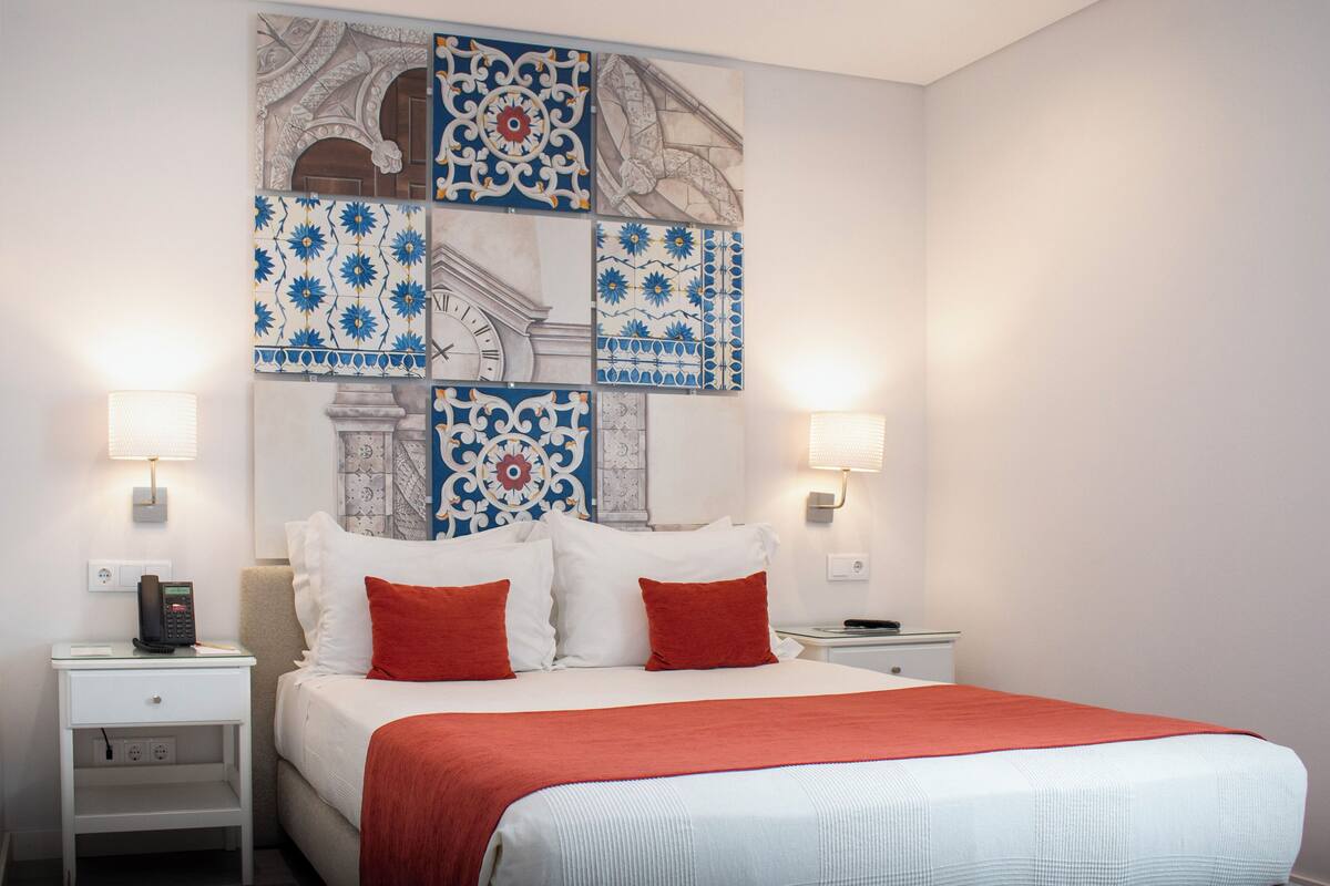 A hotel room with a large bed, two nightstands, a wall clock, and decorative tiles.