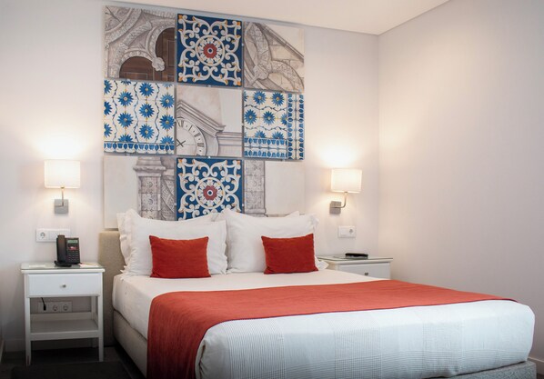 A hotel room with a large bed, two nightstands, a wall clock, and decorative tiles. - Rio Art Hotel (Setubal)