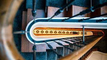 A spiral staircase with a wooden handrail and black balusters, leading to a landing with a patterned floor.