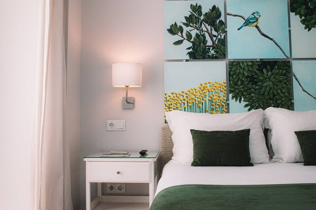A neatly arranged bedroom with a bed, a bedside table, a lamp, and a wall with artwork.