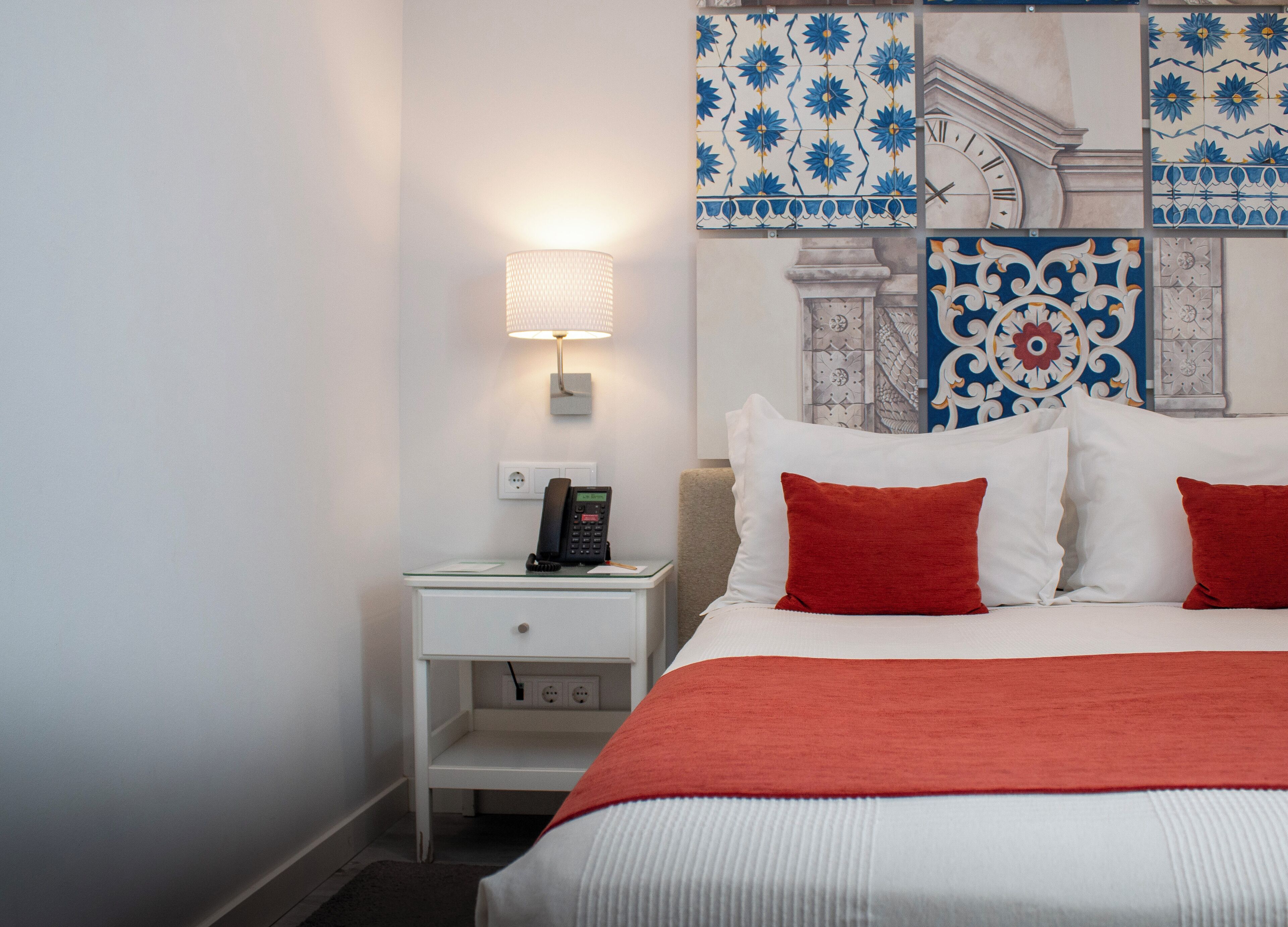 A hotel room with a bed, white nightstand, lamp, and decorative wall tiles.