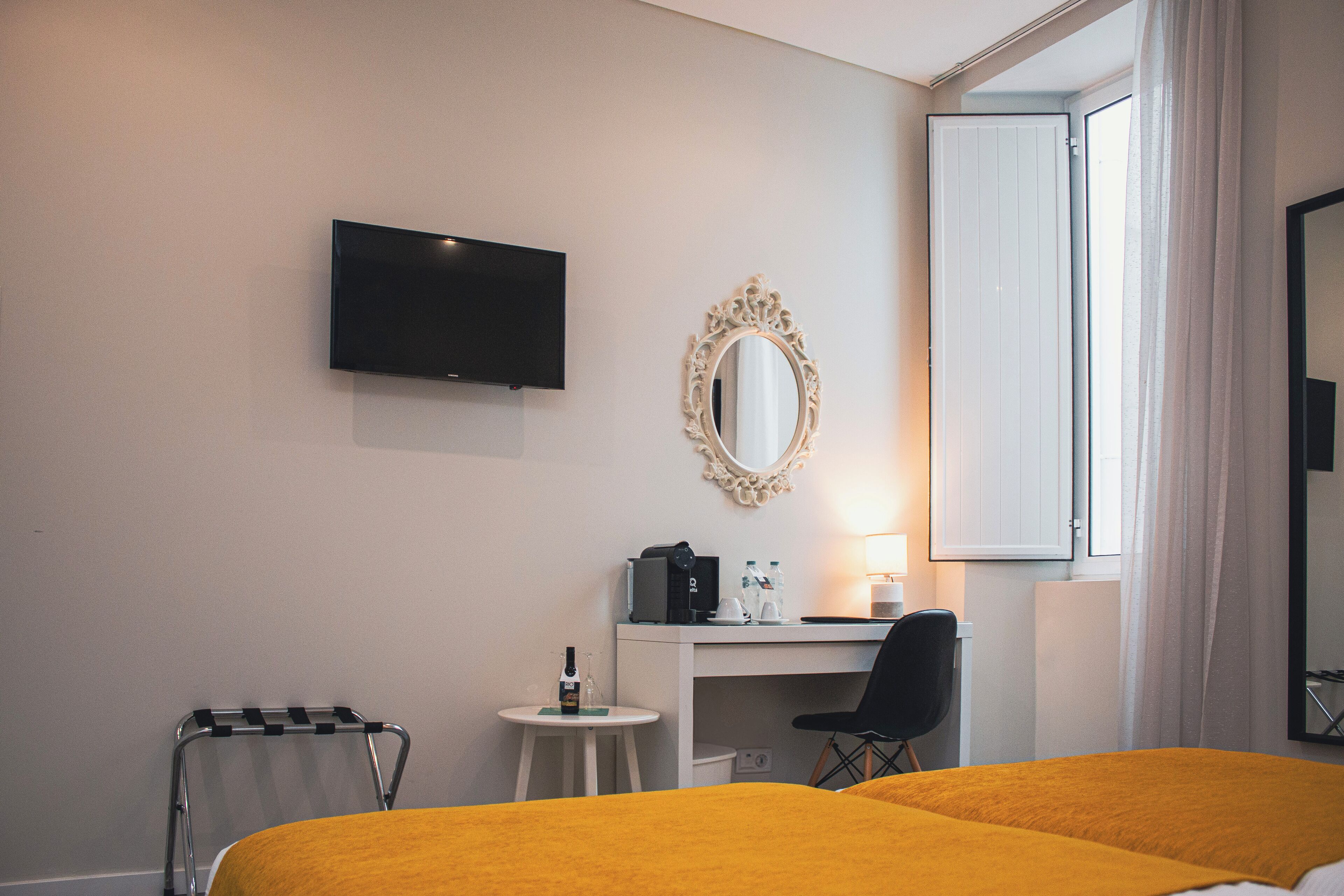 Habitación de hotel con cama, escritorio, silla, televisor, espejo y ventana con cortinas.