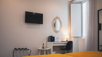 Habitación de hotel con cama, escritorio, silla, televisor, espejo y ventana con cortinas.