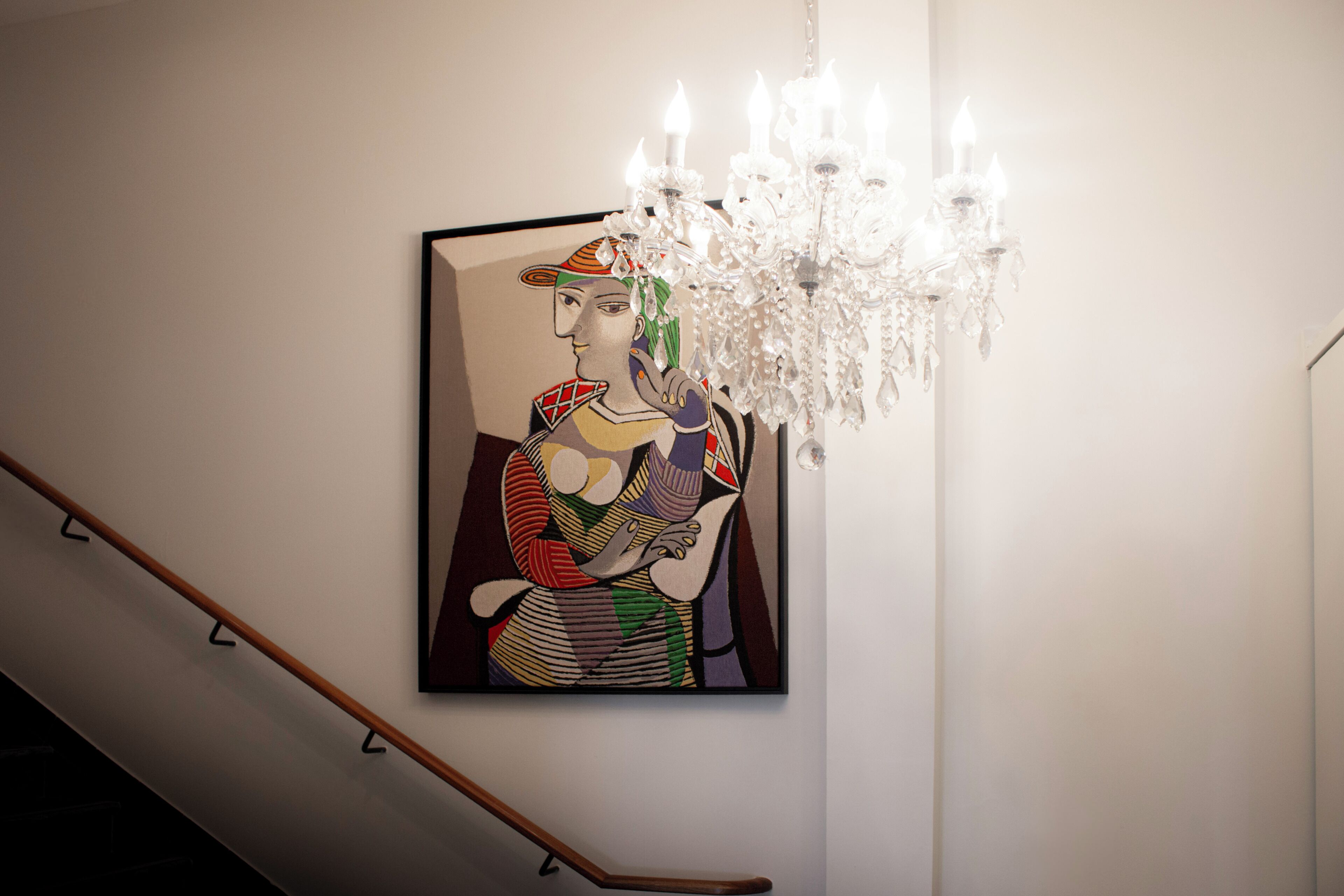 A staircase with a wooden handrail and a wall-mounted painting of a figure holding a child.