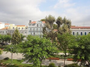 Uma fileira de edifícios históricos com varandas, uma praça pavimentada e árvores em primeiro plano.