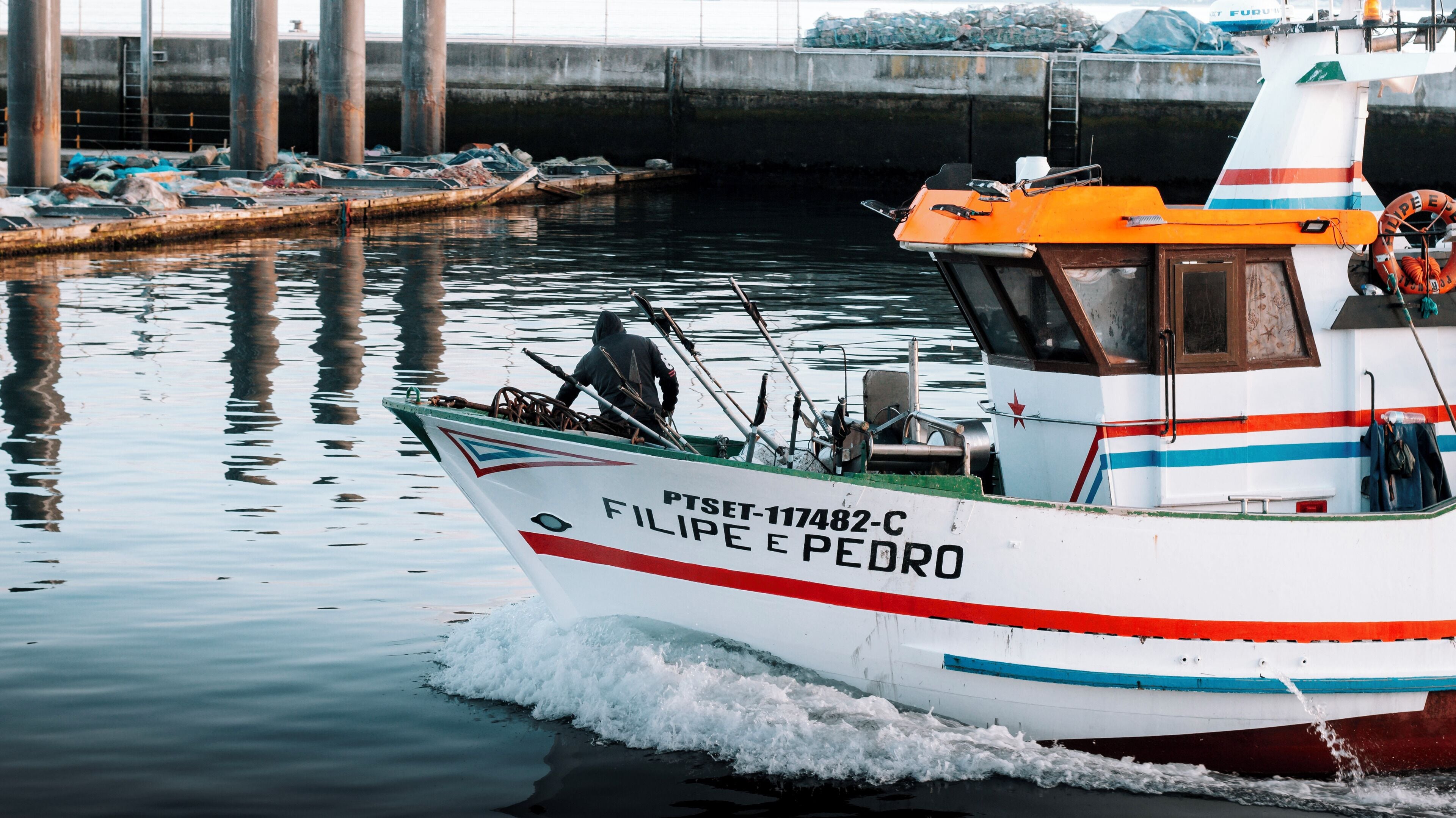 A boat named PTSET-117482-C FILIPE E PEDRO docked at a harbor with a concrete pier in the background.