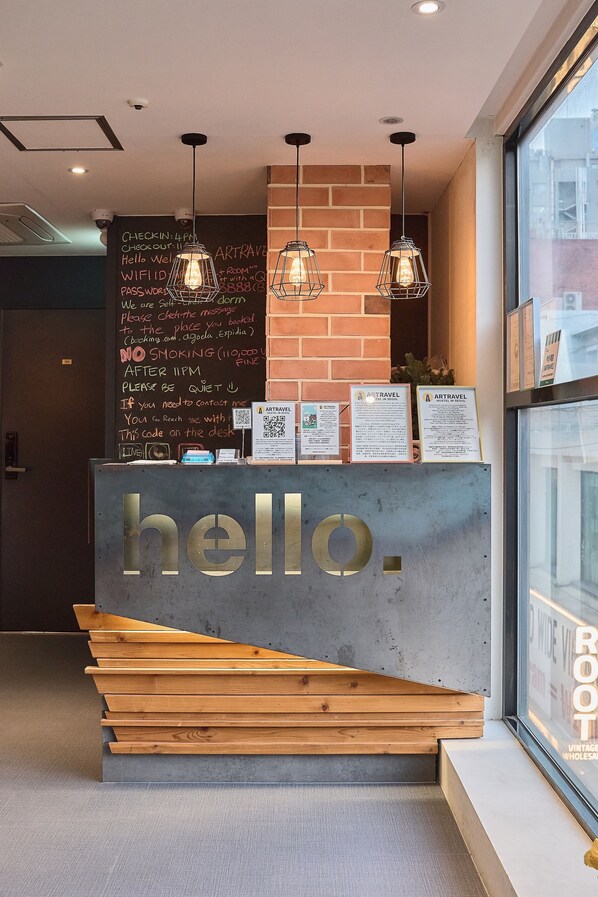 A reception desk with a 'hello' sign, a chalkboard with information, and hanging pendant lights.