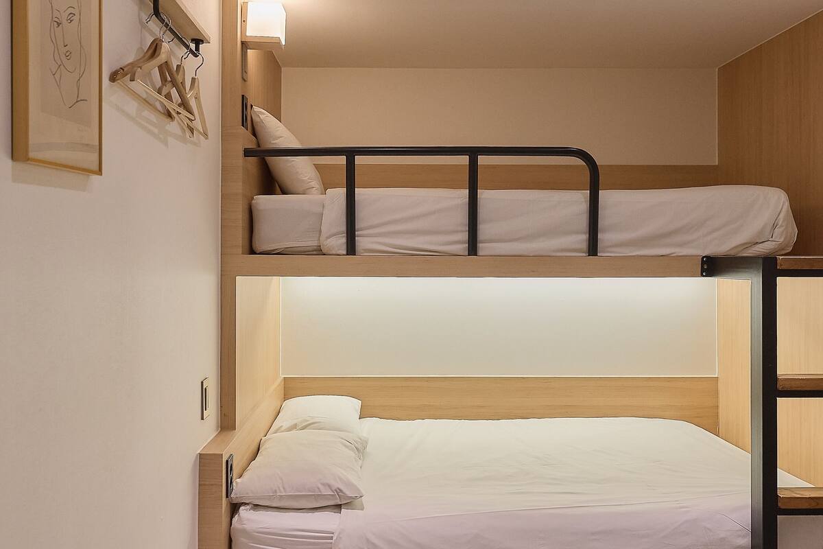 Een slaapkamer met stapelbed, een lichtgekleurde vloer, een wandlamp en een ingelijste foto.