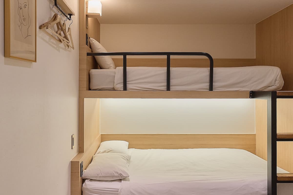 A bunk bed room with a light-colored floor, a wall-mounted light fixture, and a framed picture.
