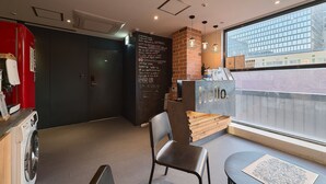 Een hotel lobby met een receptiebalie, een zithoek, een wasmachine en een groot raam met uitzicht op de stad.