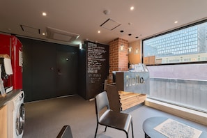 A hotel lobby with a reception desk, a seating area, a washing machine, and a large window with a city view.