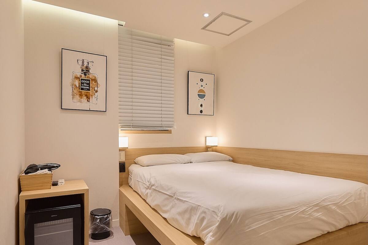 Een moderne hotelkamer met een houten bed, een nachtkastje, een klein bureau met een lamp en een schilderij aan de muur.
