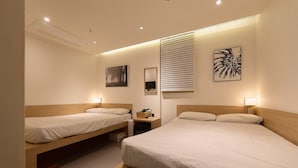 Een hotelkamer met twee bedden, een nachtkastje met lamp, een televisie aan de muur en een raam met zonwering.
