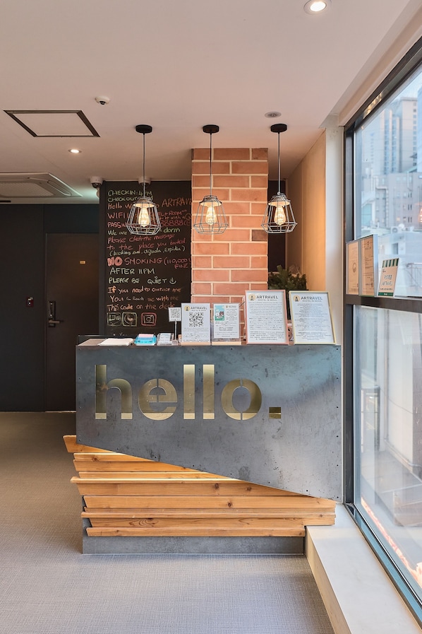 A reception desk with a 'hello.' sign, a chalkboard with information, and hanging pendant lights.