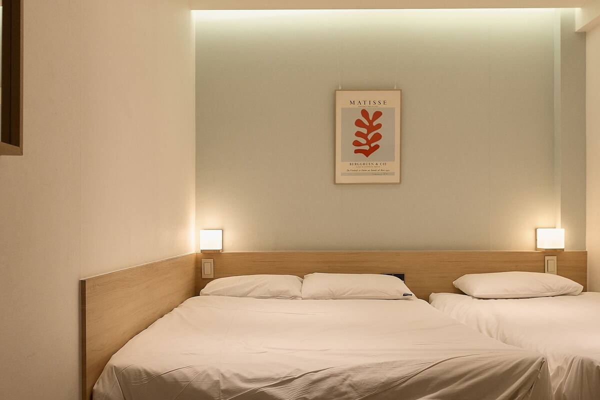 Een slaapkamer met een houten hoofdeinde, twee nachtkastjes met lampen, een lijstwerk aan de muur en een bankje onder het bed.
