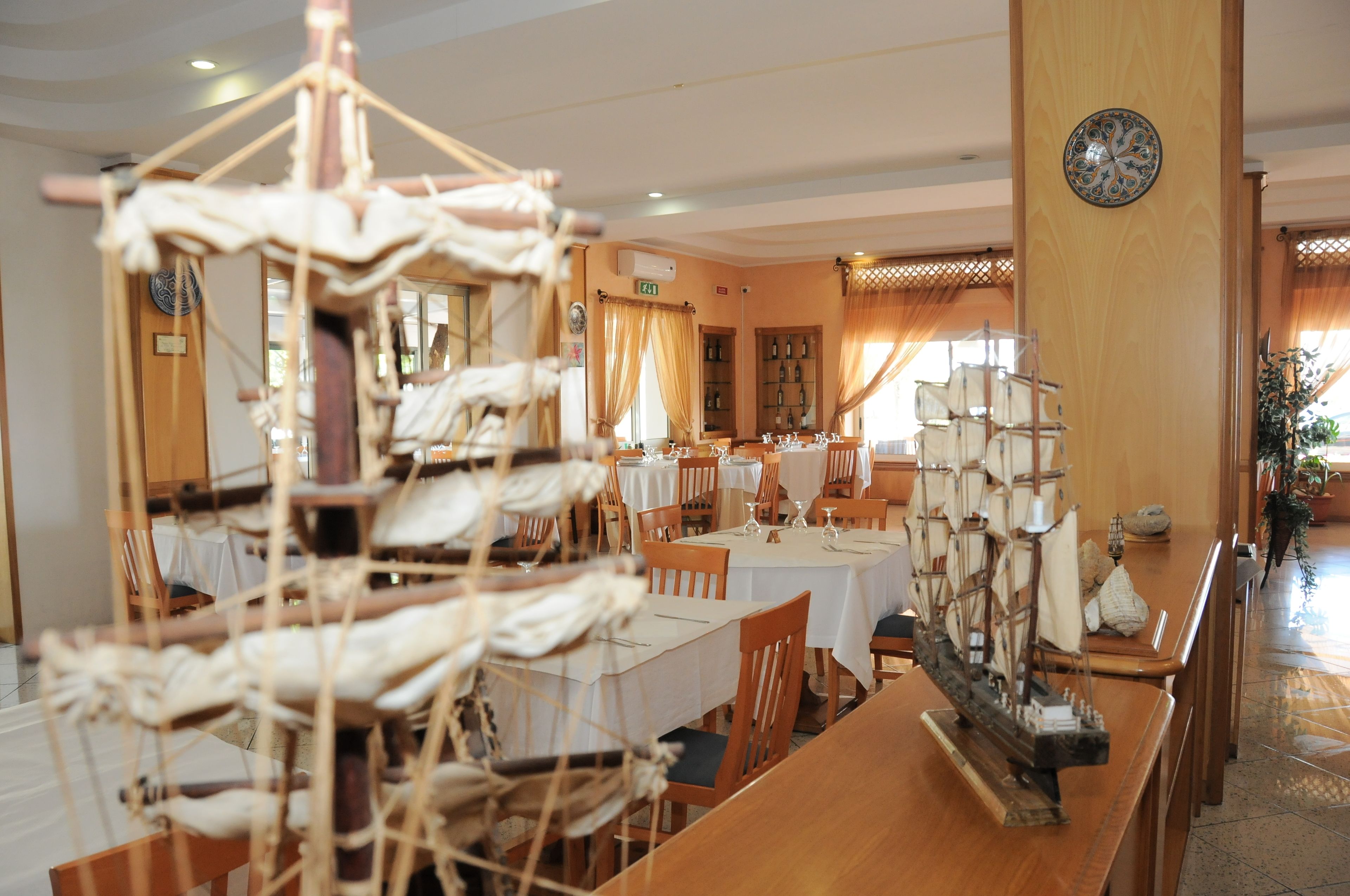 Un comedor con mesas dispuestas para el servicio, un modelo de barco y un reloj en la pared.