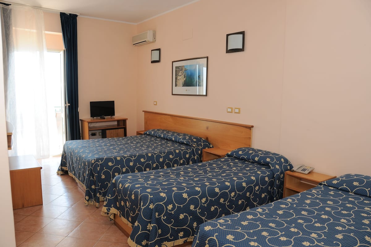 A hotel room with three beds, a TV, and a window with curtains.