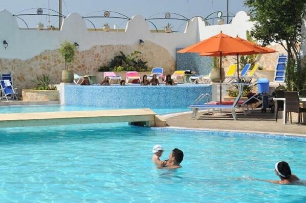 Una piscina al aire libre, sombrillas, sillones reclinables de piscina