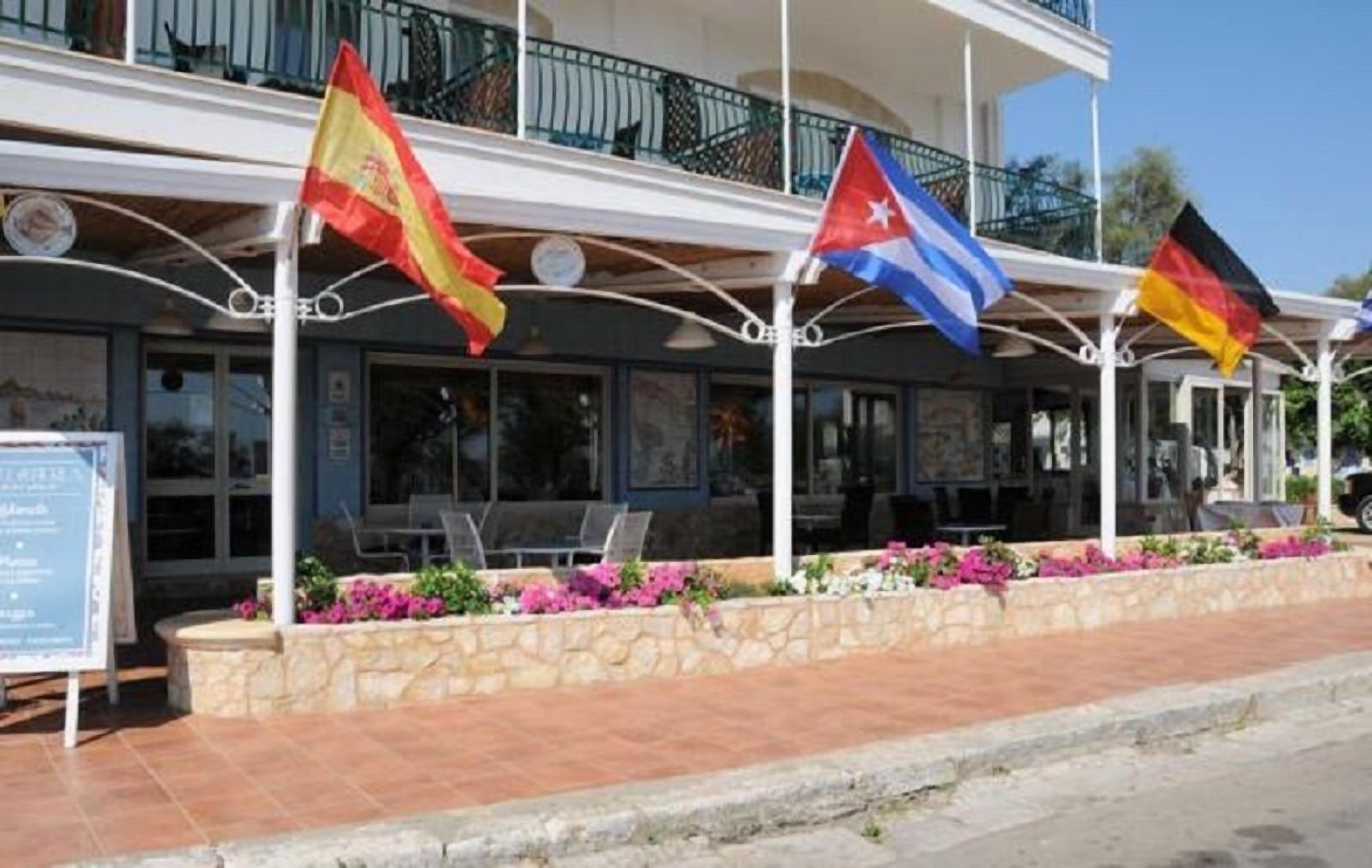 A building with multiple balconies, outdoor seating, and flags of Spain, Cuba, and Germany.