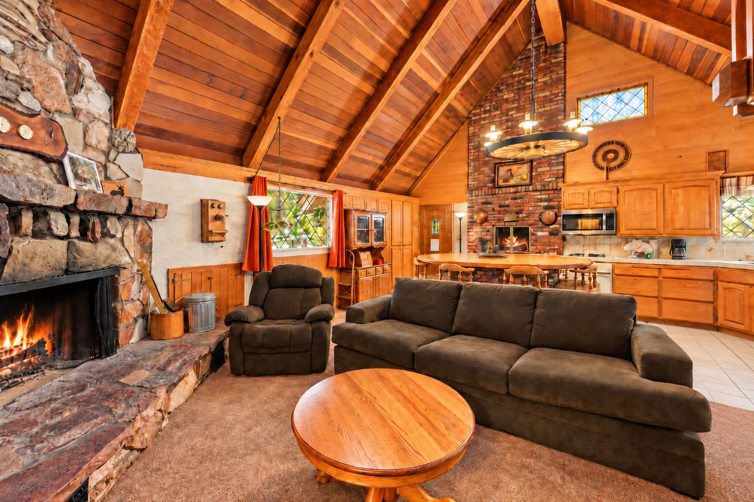 A cozy living room with a fireplace, a stone wall, and a high ceiling with wooden beams.