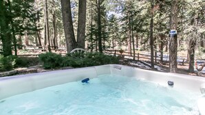Ein Whirlpool, umgeben von bewaldeter Landschaft mit hohen Bäumen und einem Holzzaun.