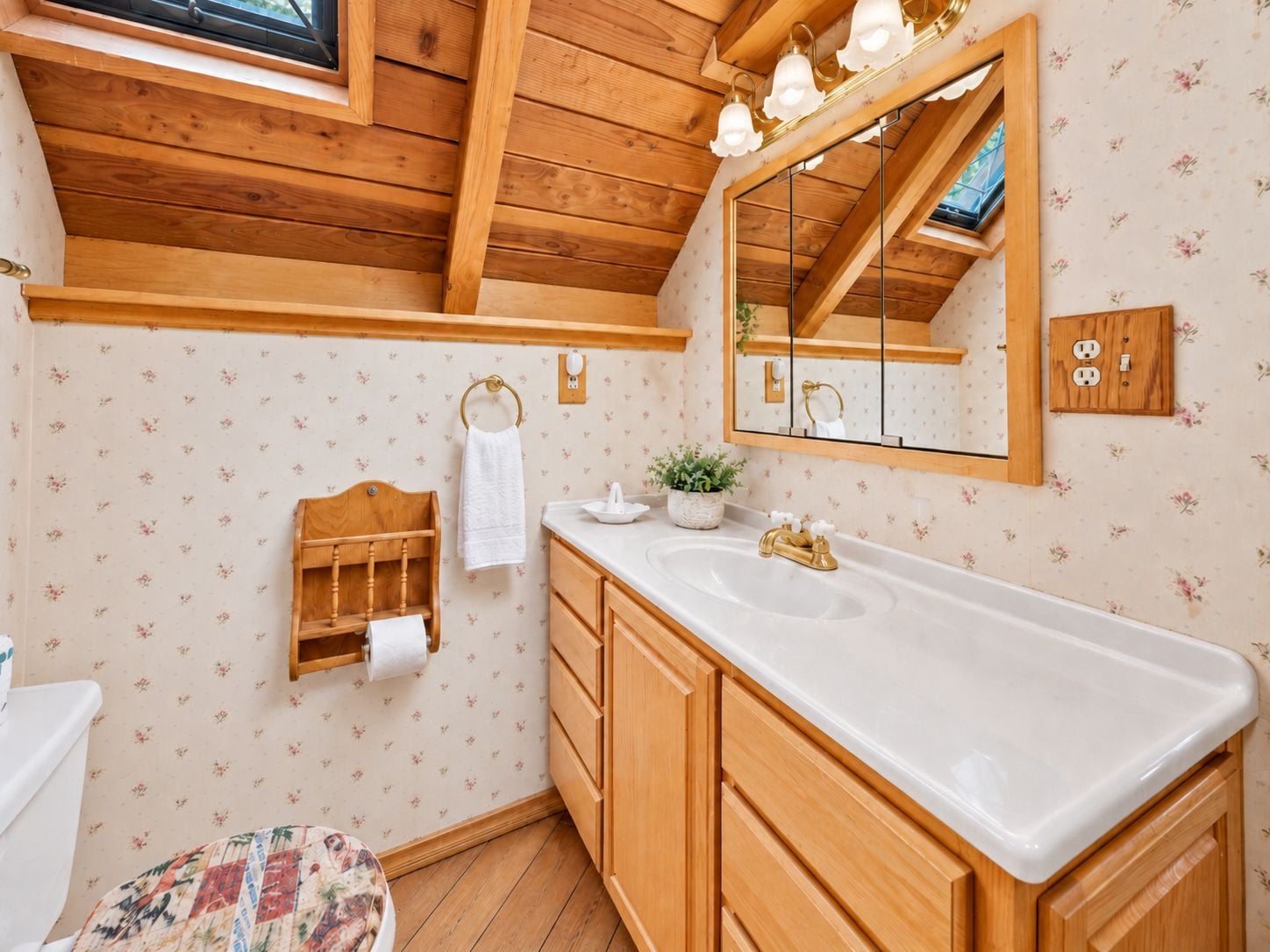 A bathroom with wooden ceiling beams, a large mirror, a white sink, and a wooden bench.