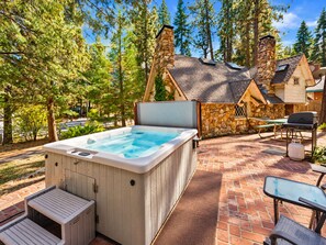 A hot tub with a stone exterior, surrounded by a patio with brick flooring and outdoor furniture. - Cornerstone Cabin (Big Bear Lake)
