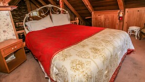 Ein hölzernes Himmelbett mit roter und goldener Bettdecke in einem rustikalen Zimmer mit Holzbalken.