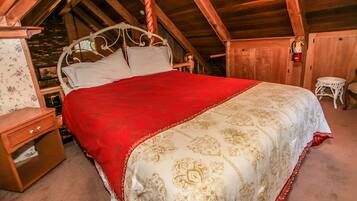 Uma cama de madeira com dossel e mosquiteiro vermelho e dourado em quarto rústico com vigas de madeira.