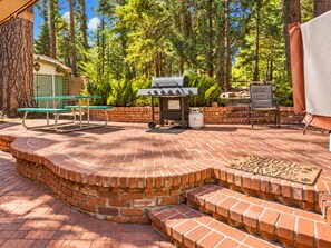 A patio with a brick fire pit, a grill, a table, and chairs. - Cornerstone Cabin (Big Bear Lake)