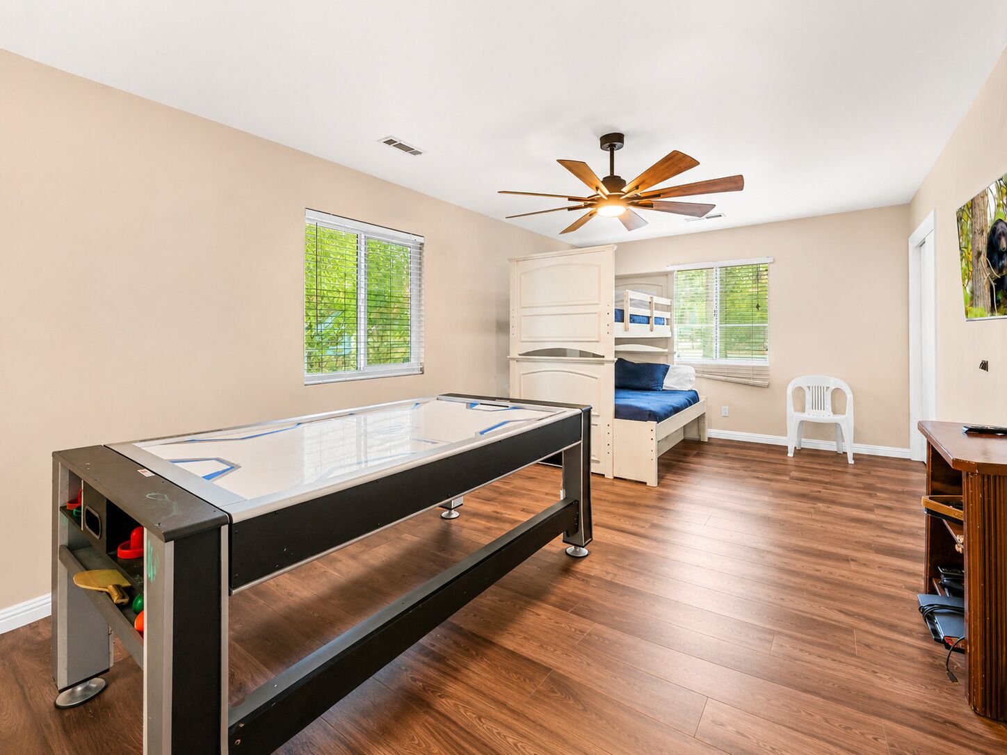Una habitación con mesa de billar, literas, ventilador de techo y ventana con persianas.