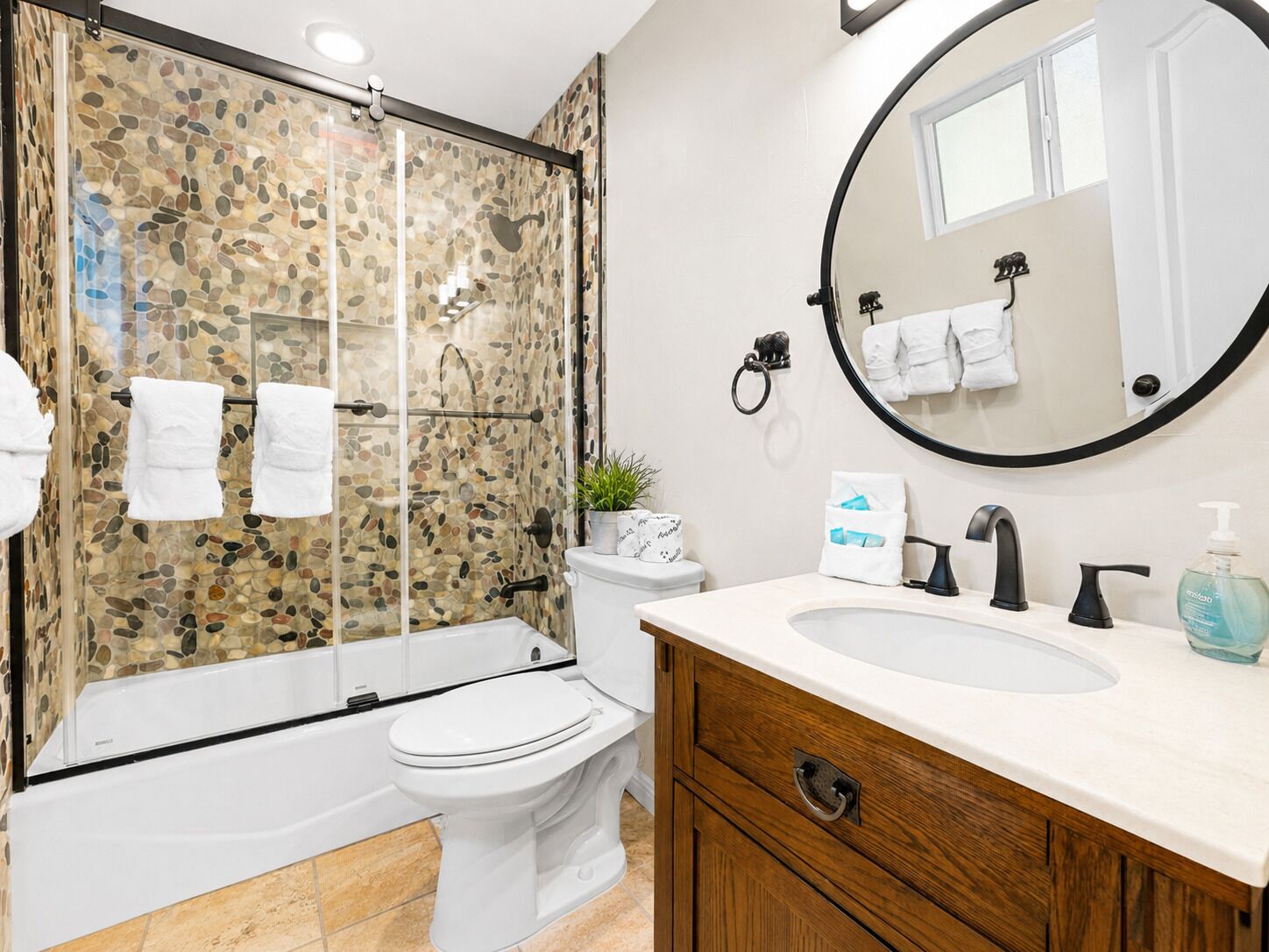 A bathroom with a glass-enclosed shower, a toilet, a sink with a mirror, and a wooden vanity.