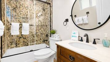 A bathroom with a glass-enclosed shower, a toilet, a sink with a mirror, and a wooden vanity.