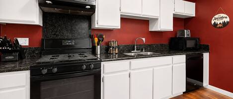 A kitchen with white cabinets, a black stove, and a red wall.
