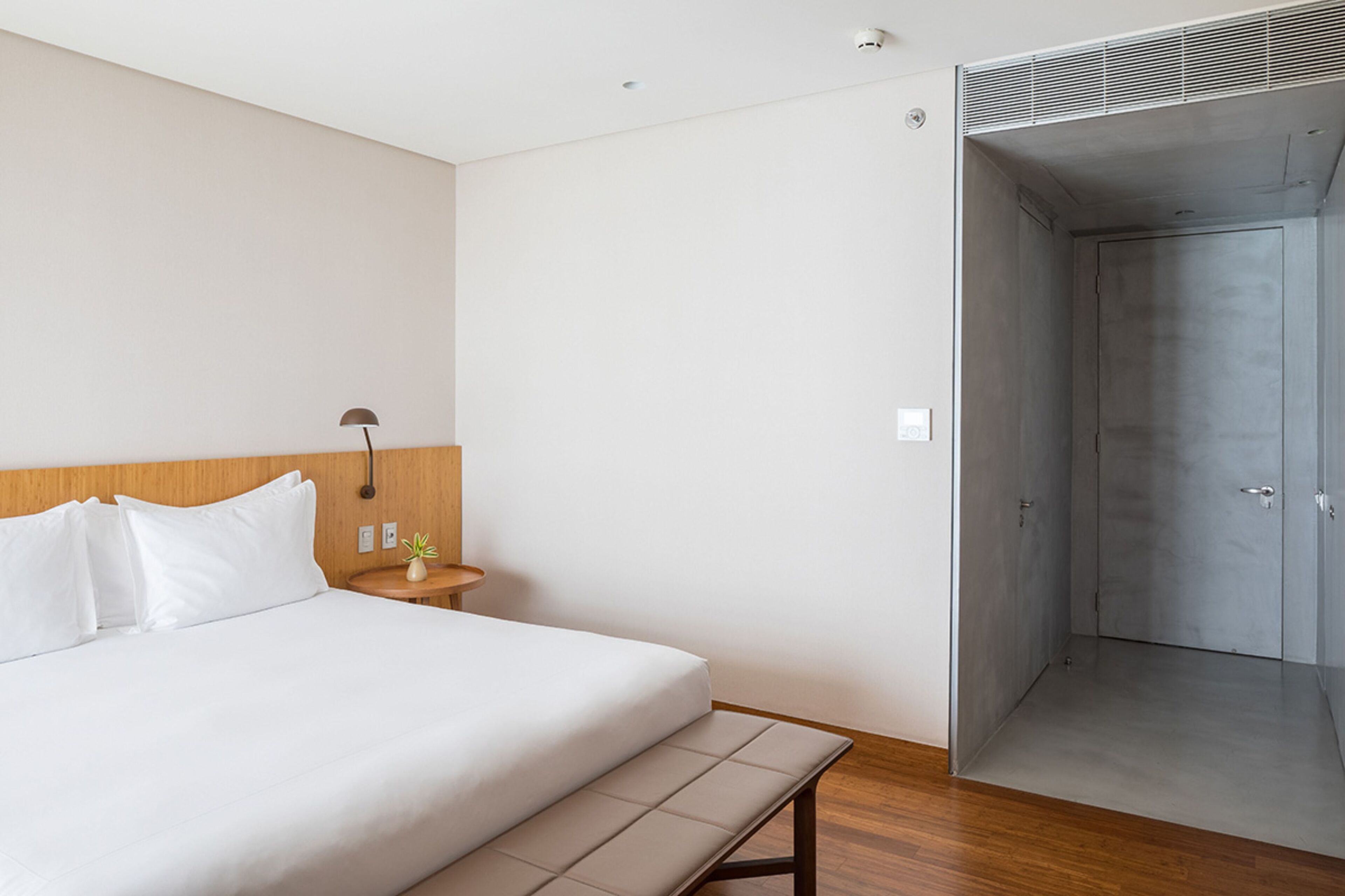 A modern hotel room with a large bed, bedside table, lamp, and a walk-in closet.