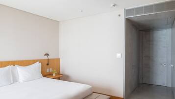 Una habitación de hotel moderna con una cama grande, mesita de noche, lámpara y vestidor.
