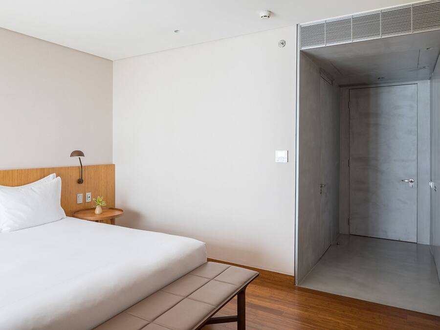 Une chambre d’hôtel moderne avec un grand lit, une table de chevet, une lampe et un dressing.