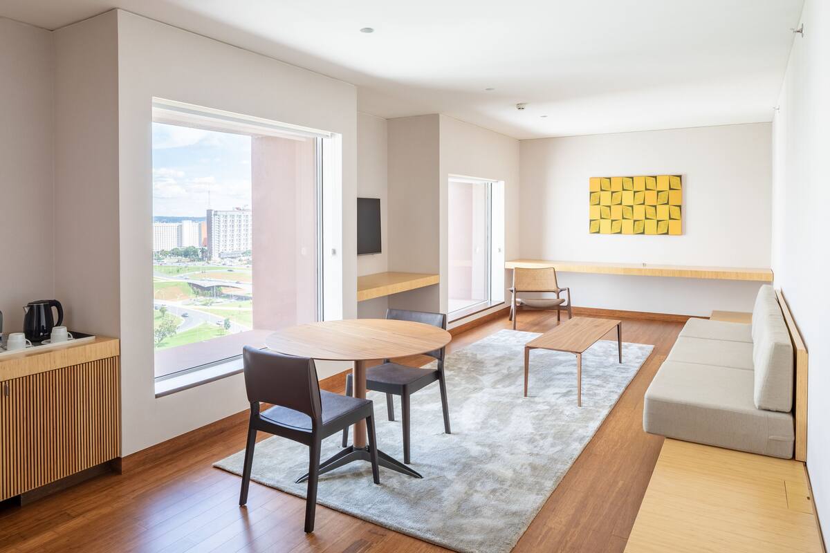 Een moderne woonkamer met een houten eettafel, twee stoelen, een bank en een groot raam met uitzicht op de stad.