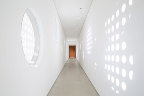 Ein moderner, minimalistischer Flur mit hellem Boden und Wänden, mit runden Aussparungen an der rechten Wand und einer großen, runden Aussparung an der linken.