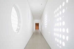 Un pasillo moderno y minimalista con suelo y paredes de color claro, con aberturas circulares a la derecha y un gran círculo a la izquierda.