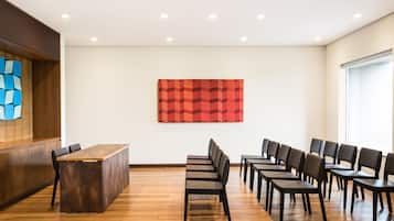 Un salón de conferencias con una mesa y sillas de madera, un cuadro abstracto rojo en la pared y una ventana a la derecha.