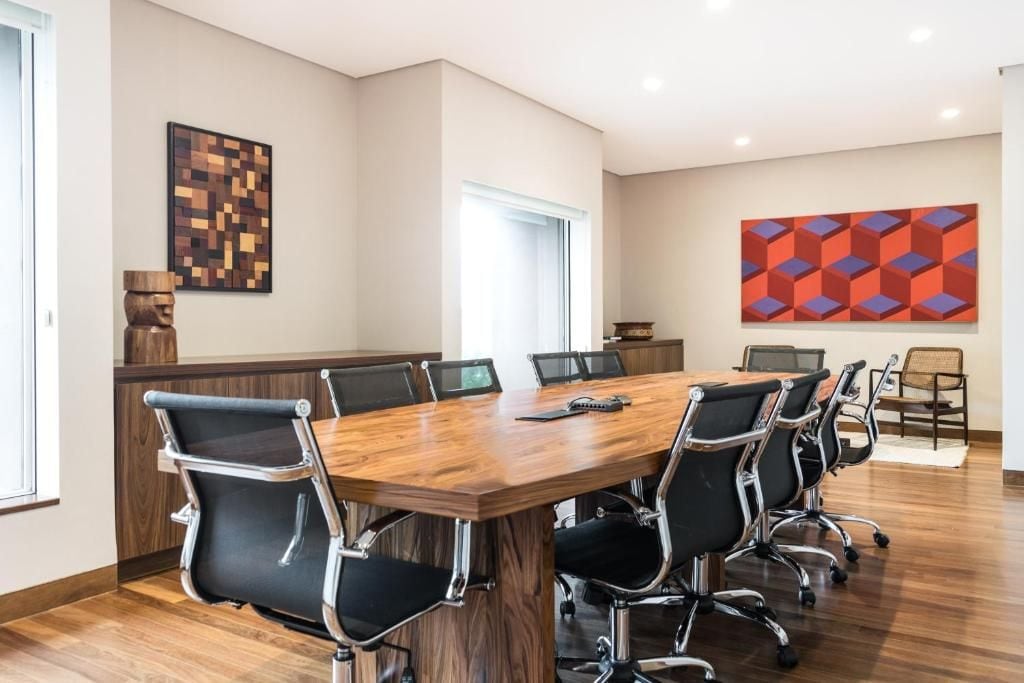 Uma sala de conferências com mesa de madeira, cadeiras pretas e duas pinturas abstratas nas paredes.